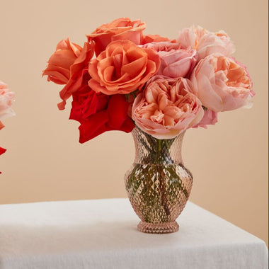 Vase with red and pink flowers on a white surface against a beige background