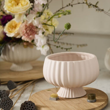 Pink ceramic bowl on a wooden stand with flowers and decorative items in the background