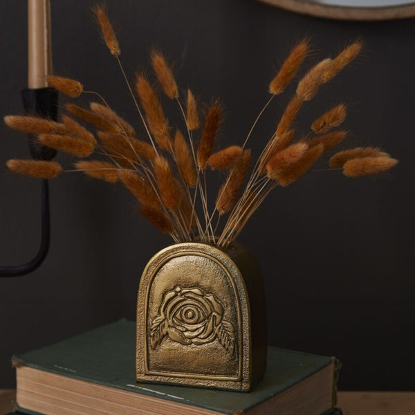 Bronze vase with dried grasses on top of two books against a dark background