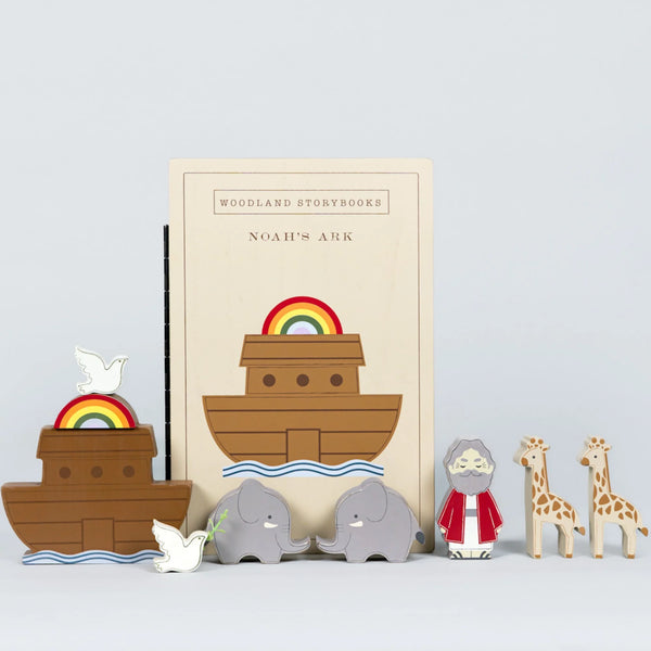 Wooden Noah's Ark storybook set on a light gray background, featuring a tall book with an ark illustration, a wooden ark, a dove, two elephants, a wise man figure, and two giraffes.
