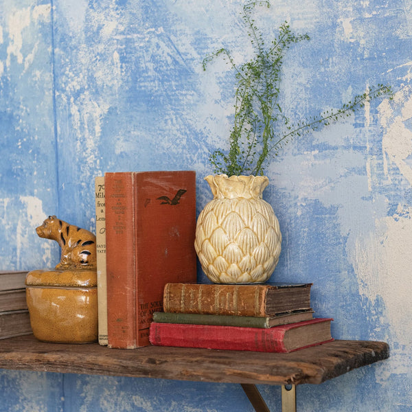 Wooden shelf with books and a vase against a textured blue wall